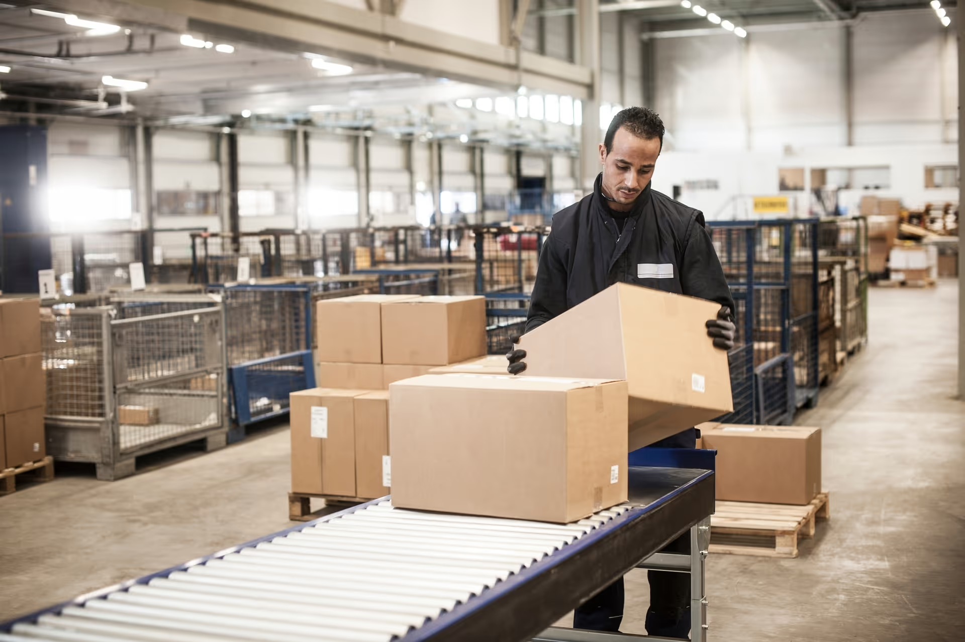 A worker manually loads parcels onto a conveyor line, representing the physically demanding, high-turnover tasks Logibot's robotic labor platform targets.
