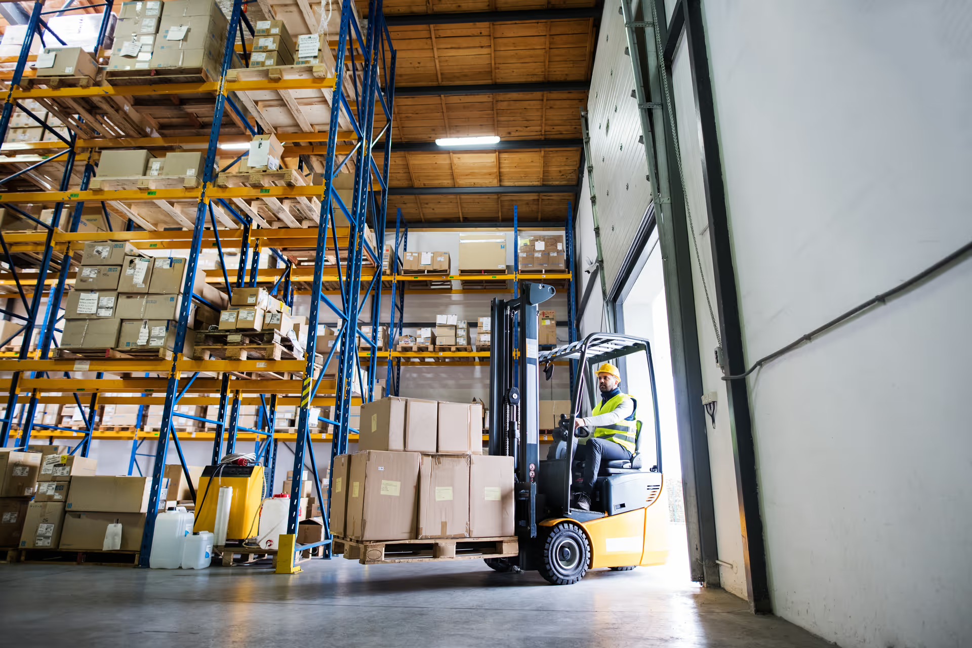 A forklift operator moves palletized goods at a warehouse loading dock, illustrating the manual material handling still common in European logistics facilities.